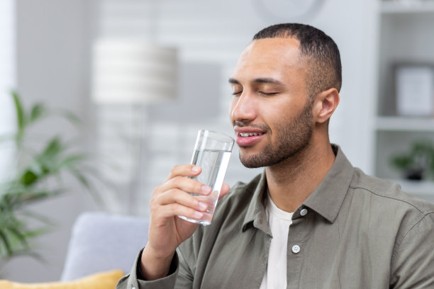 一位年轻的非裔美国男人手持透明玻璃杯闭着眼睛喝水的特写照片图片下载