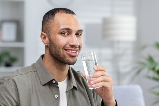 年轻的非洲裔美国男人坐在沙发上，拿着一杯水看着镜头微笑的特写照片图片下载