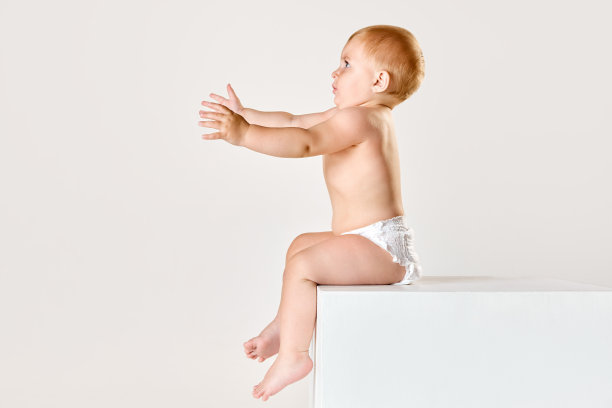 小漂亮婴儿的肖像，穿着尿布的蹒跚学步的孩子平静地坐着，看着和玩着白色的工作室背景图片下载