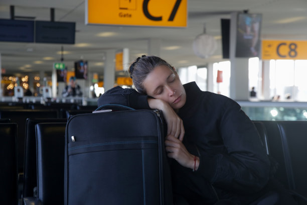 疲惫的女游客在机场候机时睡在行李上图片下载