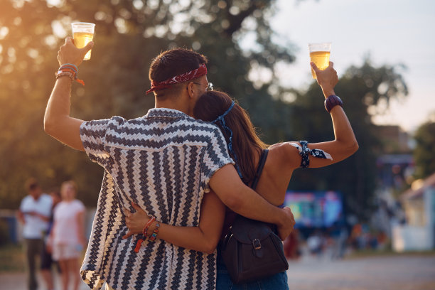 在夏季音乐节上，拥抱的夫妇喝啤酒的背影。图片下载