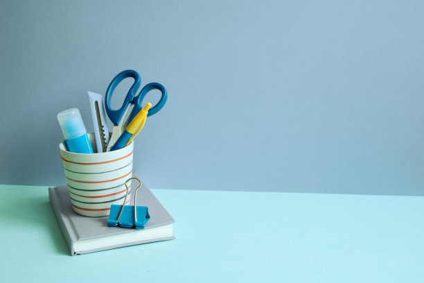 书写用品，笔筒和笔记本在蓝色的桌子上。蓝色墙壁背景。工作空间图片下载