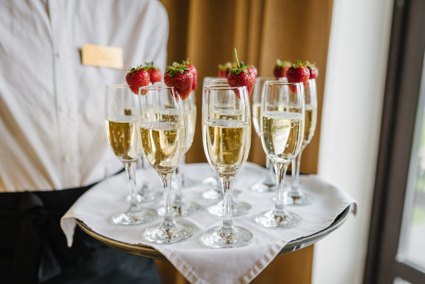 服务员端来了一盘香槟和草莓。派对和节日庆祝的概念。餐饮服务理念。一个女人拿着起泡酒。特写镜头。图片下载