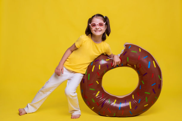 穿着黄色t恤和白色裤子的小女孩在明黄色背景下的充气环上放松图片下载