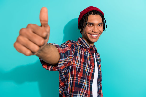 照片积极满意的人与玉米辫穿着格子衬衫显示拇指向上你的好工作孤立的蓝绿色背景图片下载