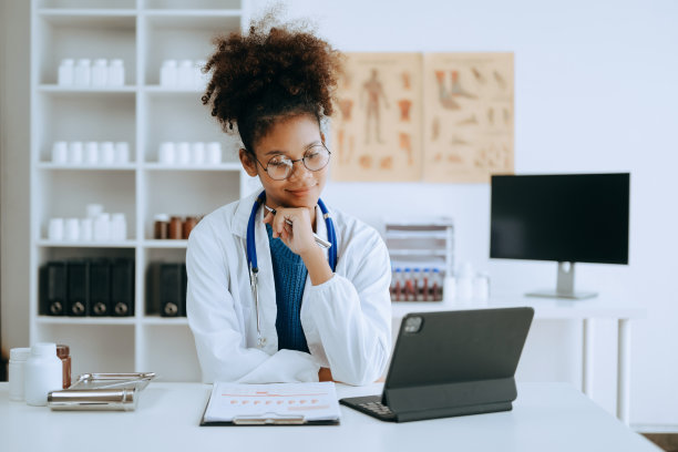 微笑的非洲男医生或顾问坐在办公桌前，写病假条、手术计划和处方，以及办公室里的临床报告测试结果，看着镜头图片下载