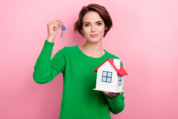 照片心情好可爱的女士穿绿色套头衫买新房上升钥匙孤立的粉红色背景图片下载