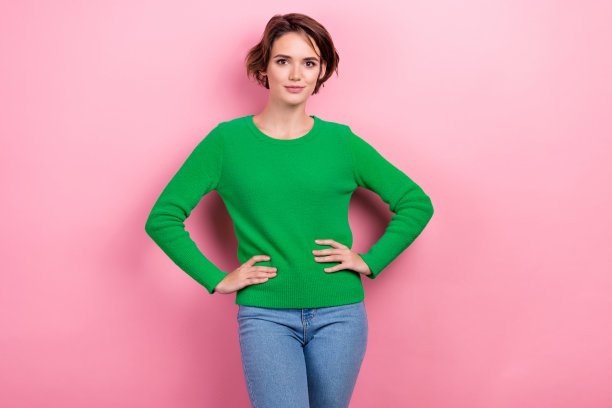 积极可爱的女士穿着绿色时尚的衣服，在粉红色的背景上摆姿势，手放在腰上图片下载