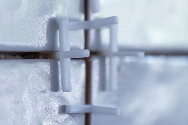 白色塑料接缝垫片的特写，放置在瓷砖之间的接缝处，瓷砖用瓷砖粘合剂安装在墙上。图片下载