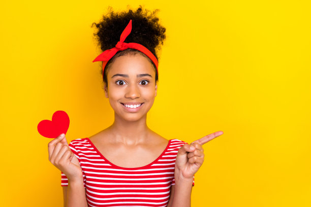 照片中漂亮闪亮的女士穿着条纹红色t恤，心牌上升，手指指向空白空间，孤立的黄色背景图片下载