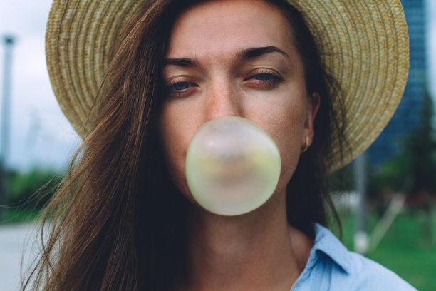 戴着帽子的年轻美女在户外吹着口香糖泡泡图片下载