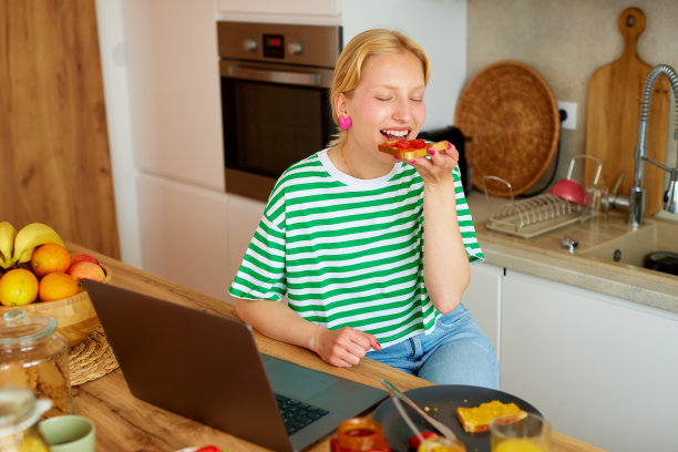 年轻女子一边使用笔记本电脑，一边在家享用早餐图片下载