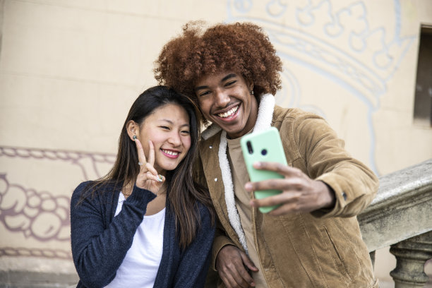 幸福的年轻情侣在户外用手机自拍。一对快乐的夫妇微笑着在外面拍照。图片下载