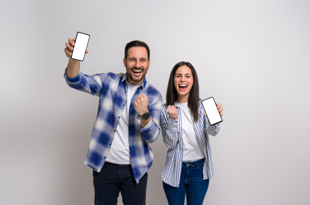 欢快的女友和男友高兴地挥舞着拳头，展示智能手机进行营销。穿着便服的年轻夫妇尖叫着庆祝他们的成就图片下载
