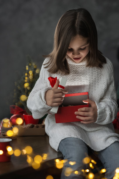 2023年圣诞快乐，新年快乐。快乐的女孩在灯光的背景下打开礼物图片下载