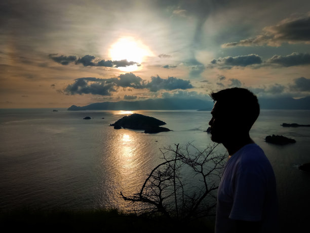 一个人在夕阳背景下的剪影，一个人在日落时站在山上看海的剪影图片下载