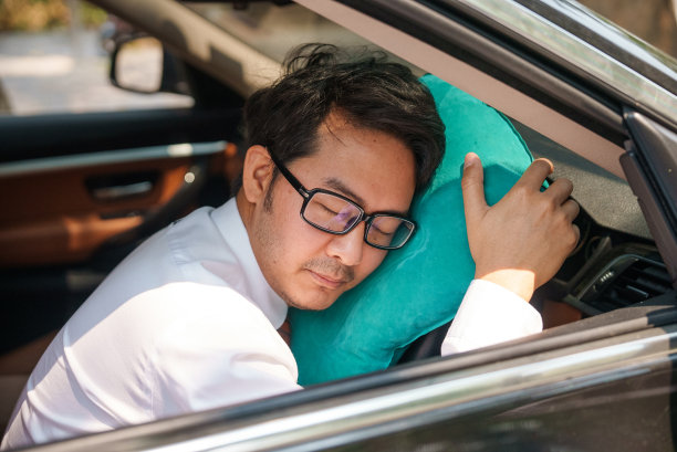 亚洲男性上班族坐在驾驶座上，头枕在方向盘上，愉快地睡在车里。图片下载