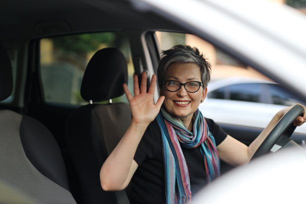 一个开着车的开朗、成熟、积极的女人在挥手。图片下载