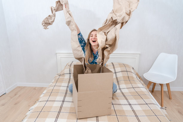 吃惊的年轻女子坐在床上打开家里的纸板箱。交付包裹图片下载