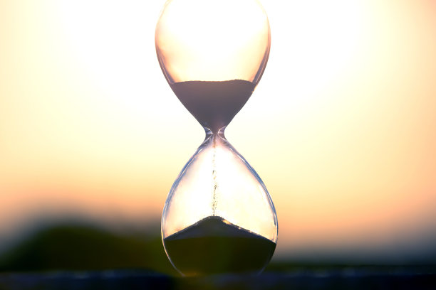 沙漏在夕阳的背景下计算时间的长度。宇宙中生命时间流动性的概念。时间和光图片下载