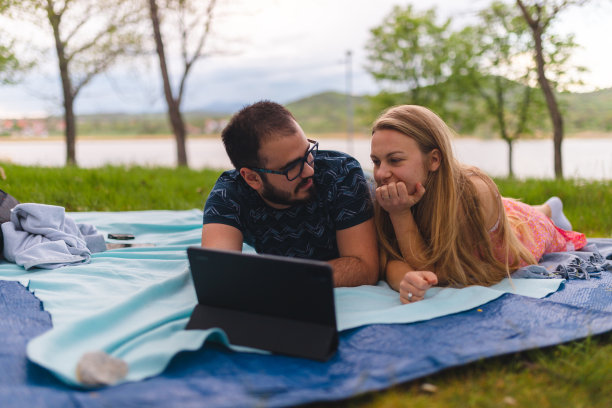 年轻浪漫的夫妇躺在野餐毯子上，在平板电脑上看电影，而在自然图片下载