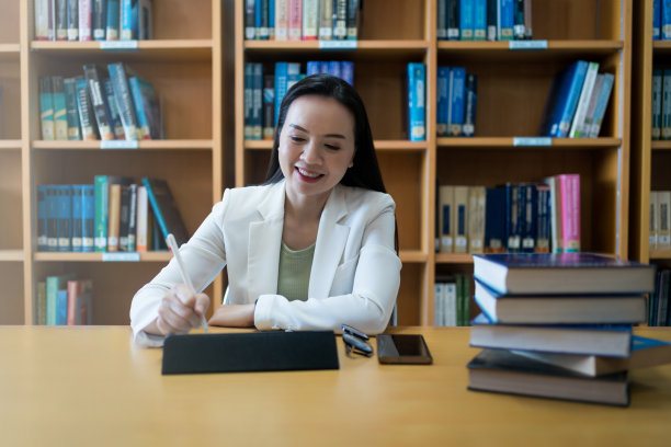 一个成熟的大学讲师在图书馆工作，桌上放着平板电脑和书图片下载