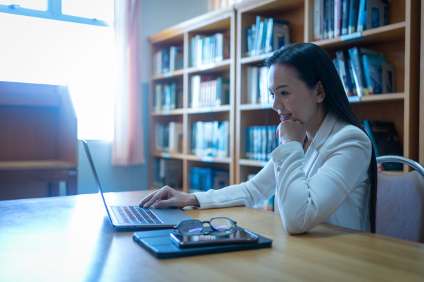 一个成熟的大学讲师在图书馆工作的肖像，桌上放着笔记本电脑和书图片下载