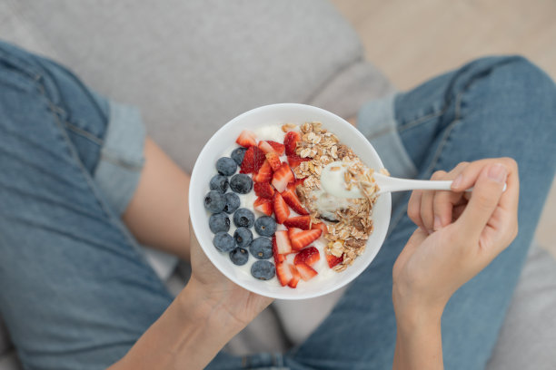 亚洲妇女在家里享用美味健康的早餐。保健女性吃酸奶配格兰诺拉麦片和浆果。健康食品，维生素，清洁饮食，节食，排毒，有机食品。图片下载