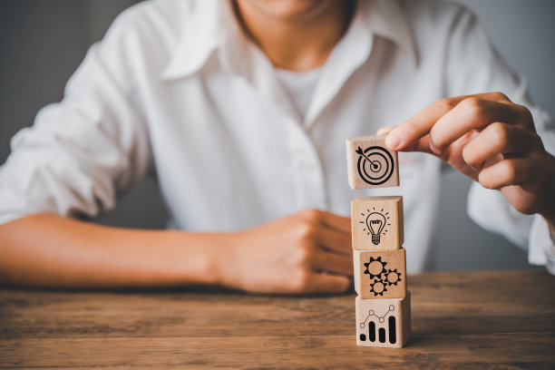 手里拿着一个木块，上面有关于商业战略和行动计划的图标，以引导商业成功的目标。企业战略的目标实现概念图片下载