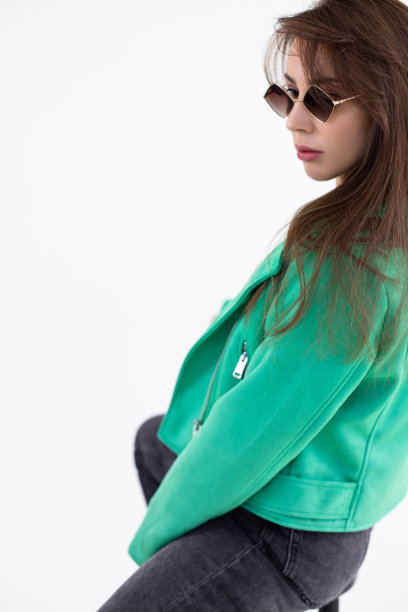 女士的肖像坐在椅子上，黑色牛仔裤和绿色夹克与太阳镜。有吸引力的女人与时尚的配件和时尚的穿着特写。时尚照片，在工作室的白色背景摆姿势图片下载