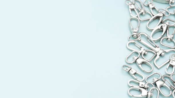 淡蓝色背景上放着一堆用来制作包和背包的金属龙虾爪扣。包、背包用镀铬金属配件及用品。手袋制作，拷贝空间图片下载