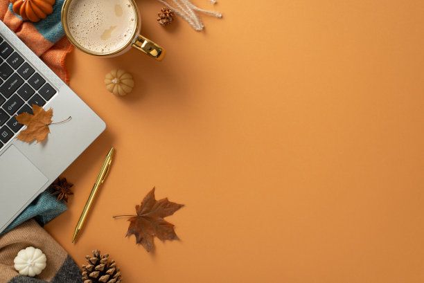 自由职业者在秋天的概念。笔记本电脑，钢笔，一杯咖啡，斑纹围巾和装饰的南瓜蜡烛，枫叶和松果在棕色孤立的背景与复制空间图片下载