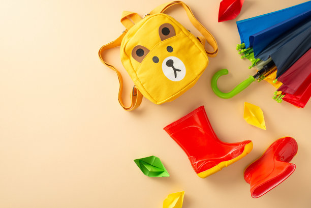 时尚的雨具在潮湿的天气孩子。从上至下的图片，在米色孤立的背景上展示了彩色雨伞、橡胶靴和黄色书包，并留出了文字或广告的空间图片下载