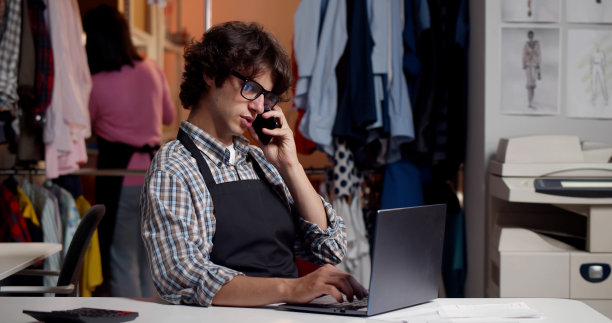 年轻的男裁缝在车间用手机与客户洽谈订单图片下载