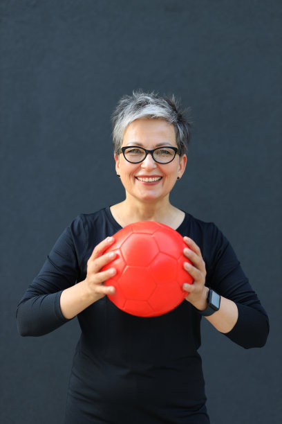 一个穿着运动服，手里拿着球的积极向上的老年妇女的肖像。图片下载