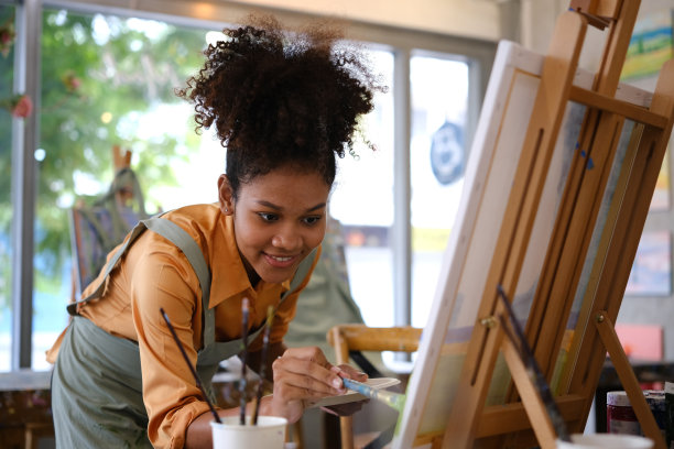 微笑的非裔美国女艺术家创作杰作，在艺术工作室用毛笔在画布上作画。图片下载