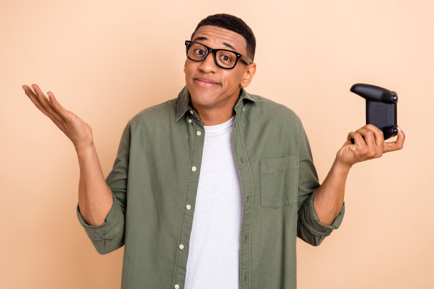 照片可疑的不确定的家伙穿着卡其色衬衫眼镜看着ps游戏孤立米色背景图片下载