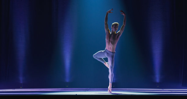 运动员在经典戏剧舞台上用戏剧性的灯光跳舞和排练脚尖旋转的广角电影镜头。优雅的古典芭蕾舞男舞者专业表演编舞图片下载