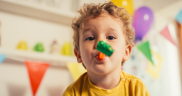 可爱的小男孩在他的生日对着镜头吹口哨的特写。快乐的幼儿庆祝和微笑。一个男孩在用气球装饰的客厅里用派对吹风机。图片下载