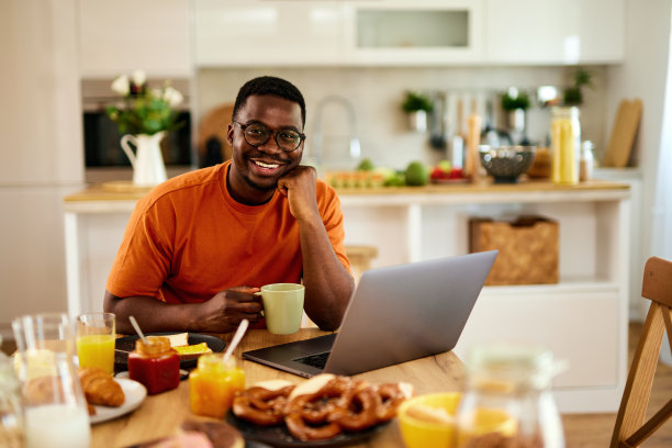 一个非裔美国人一边在家享用早餐一边使用笔记本电脑图片下载