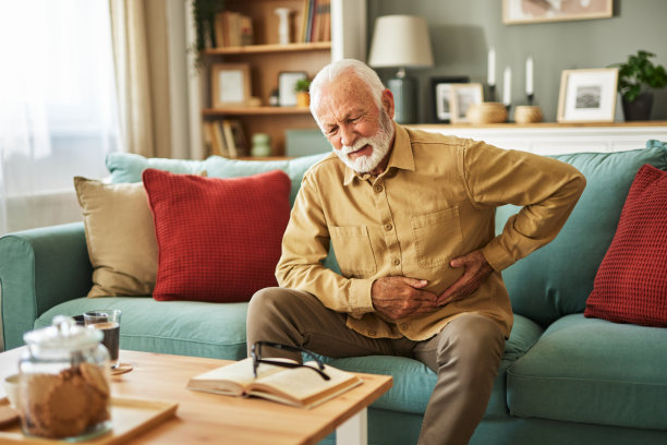 一位患胃痛的老人坐在家里客厅的沙发上图片下载