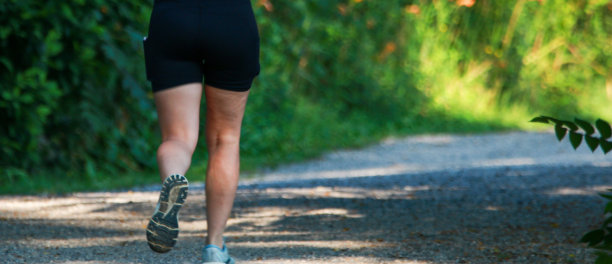 一个女人在树林里一条土路的阴凉处奔跑图片下载