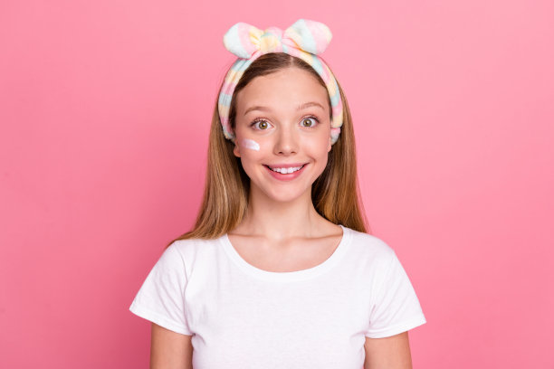 可爱的开朗的女孩的肖像，露齿微笑，脱皮乳液霜的脸，在粉红色的背景下孤立的眼睛图片下载