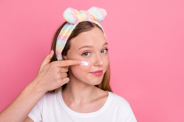 照片可爱的积极的女孩手指触摸脸脸颊应用保湿霜空白空间孤立的粉红色背景图片下载