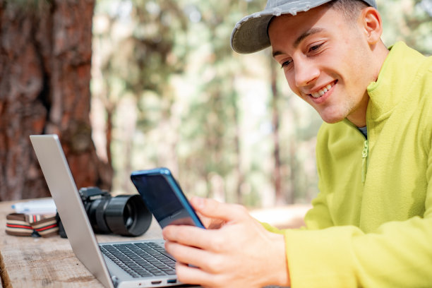 聪明的工作或在新鲜空气中学习。一个小男孩坐在森林户外的一张木桌旁，用笔记本电脑和智能手机。业务概念和工作性质图片下载