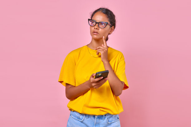 年轻体贴的印度女子手里拿着手机，摸着下巴抬起头来图片下载