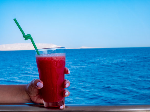 女人手持一杯水果鸡尾酒，蓝色大海为背景图片下载