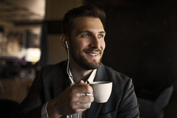 年轻微笑的商人在咖啡馆用智能手机和耳机图片下载
