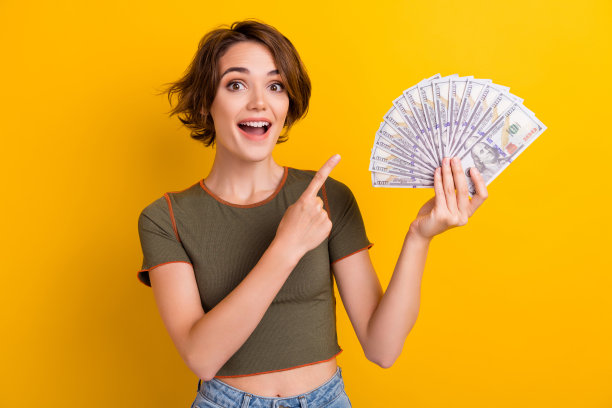 印象深刻的惊讶女人的肖像，短发，卡其色上衣，黄色背景上孤立的一束钱图片下载