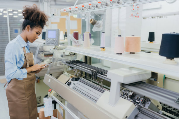 美国女裁缝设计师的半身像。在缝纫机旁用平板电脑查看产品清单。缝纫机正在生产衣服。在一个庞大的织造工业中图片下载